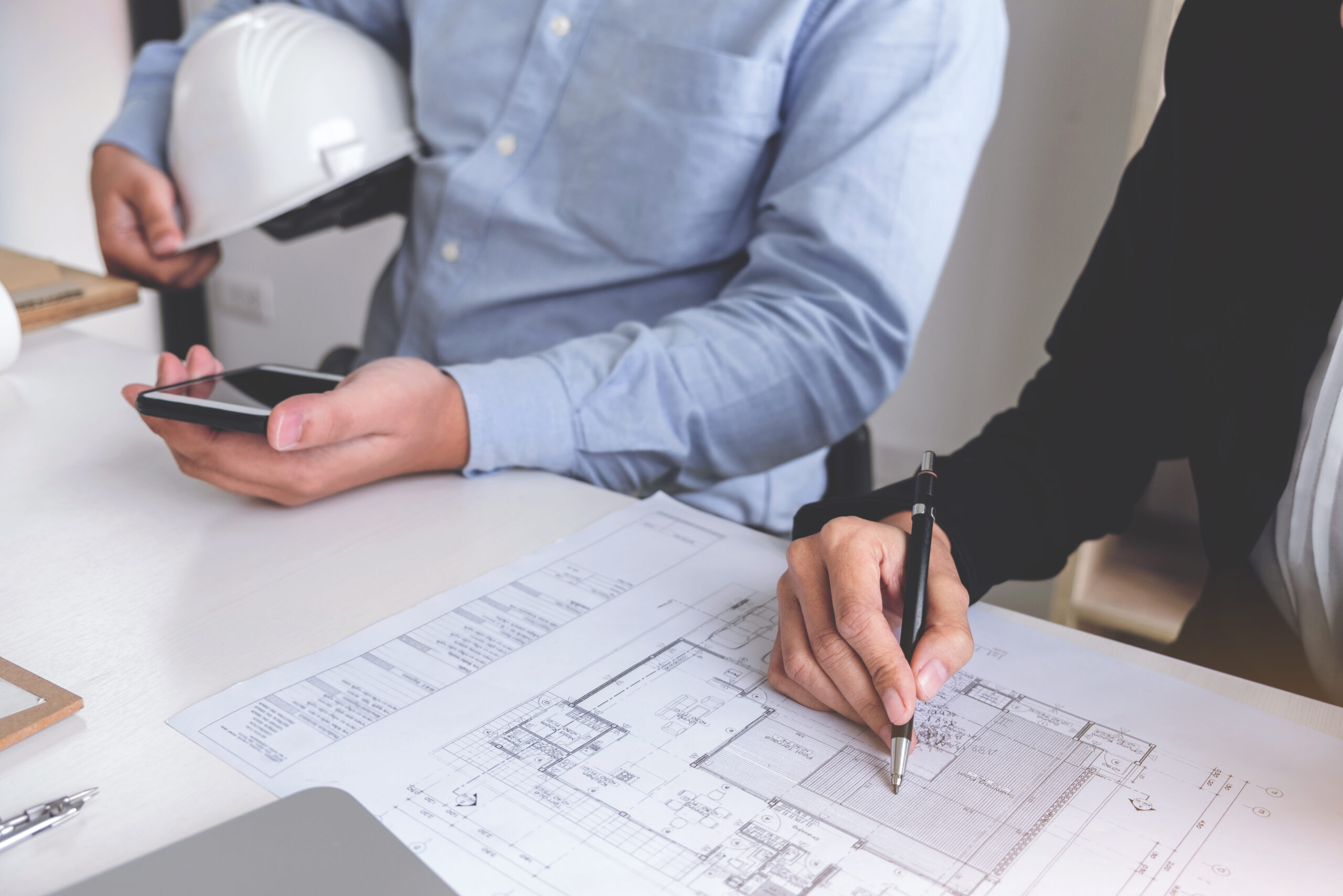 Engineering or Creative architect in construction project, Engineers hands working on construction blueprint and building model at a workplace in office, Building and architecture concept.