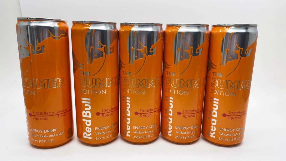 Five orange cans of Red Bull Summer Edition with strawberry and apricot flavor are lined up in a row, showcasing a vibrant energy much like the innovative world of managed IT services.