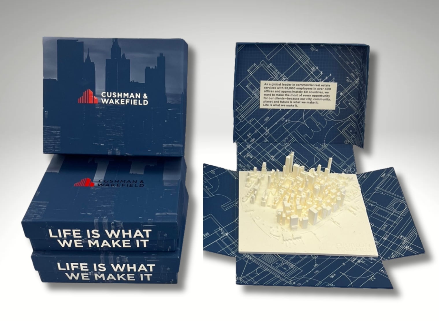 Two Cushman & Wakefield branded boxes are open to reveal white, 3D-printed cityscape models with the slogan "Life is What We Make It" on the box covers. The intricate detail showcases the precision of small format printing.