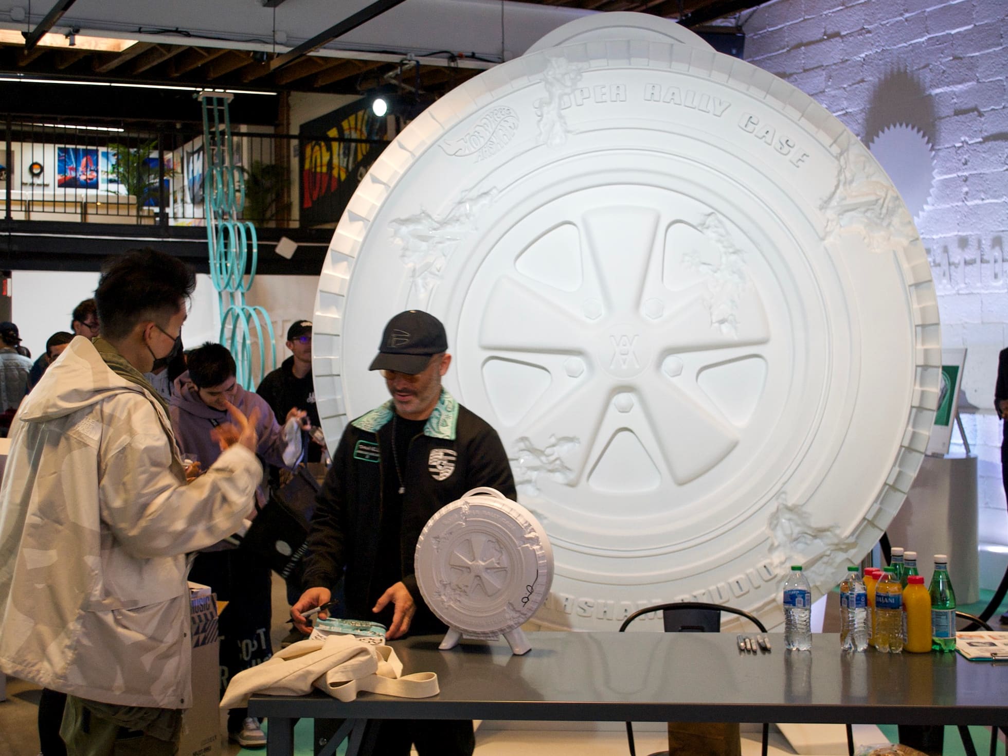 People at an event admire a large, decorative white tire-themed sculpture created using 3D printing services in the background and a smaller version on a table.