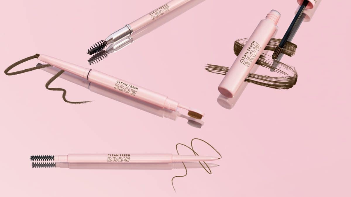 Four pink eyebrow pencils with brushes and brown swatches on a light pink background.