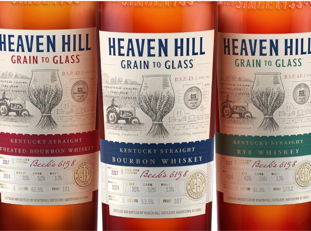 Three bottles of Heaven Hill whiskey are displayed, each with a detailed label featuring grain imagery and text specifying the type: wheated bourbon, straight bourbon, and rye whiskey.