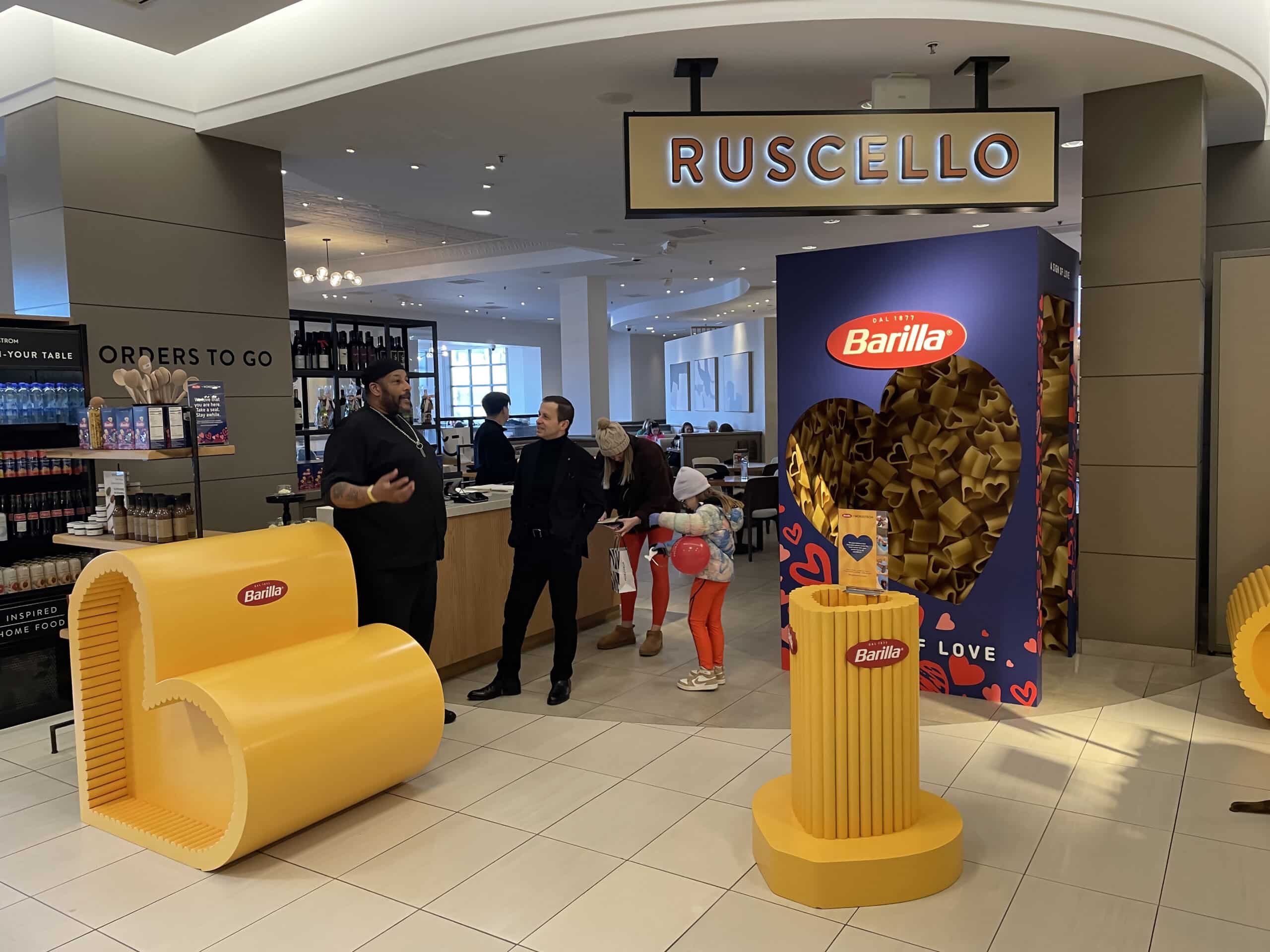People interacting in a store display area featuring large Barilla pasta packaging and seating shaped like pasta.