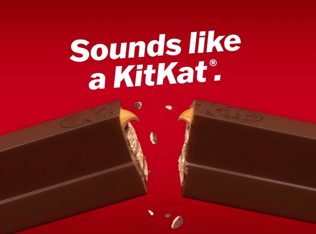 A KitKat bar snapped in half with crumbs flying, set against a red background with the text "Sounds like a KitKat.