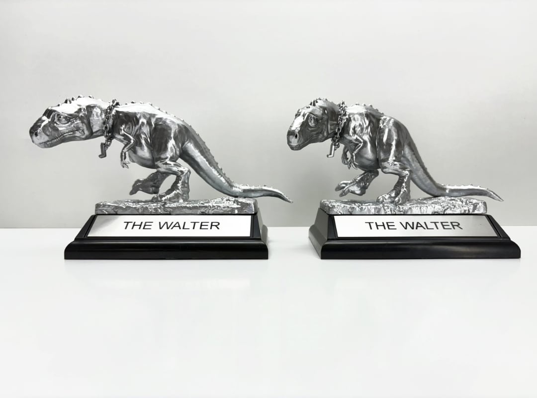 Two silver dinosaur figurine trophies labeled "THE WALTER" are displayed on a white surface with a plain background.