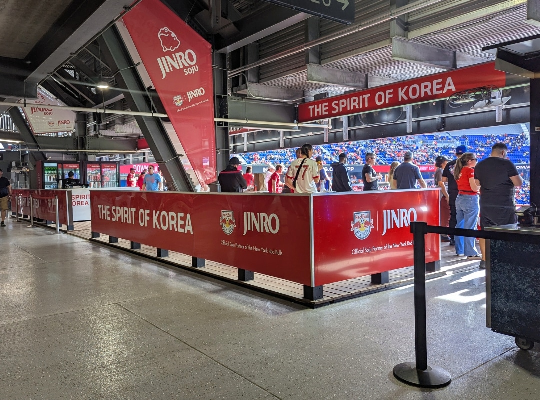 Red banners labeled "The Spirit of Korea" and "JINRO" surround a section where people stand, with a stadium and audience visible in the background.