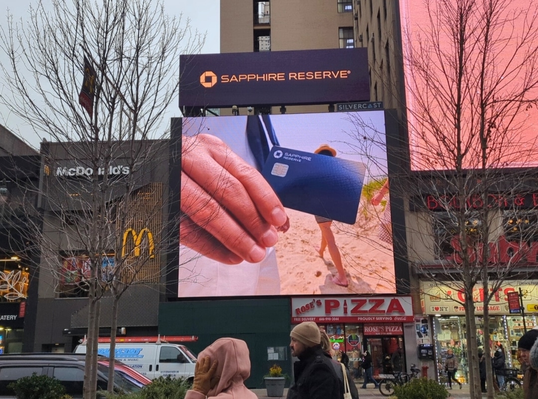 A group of people walking in front of a large screen.