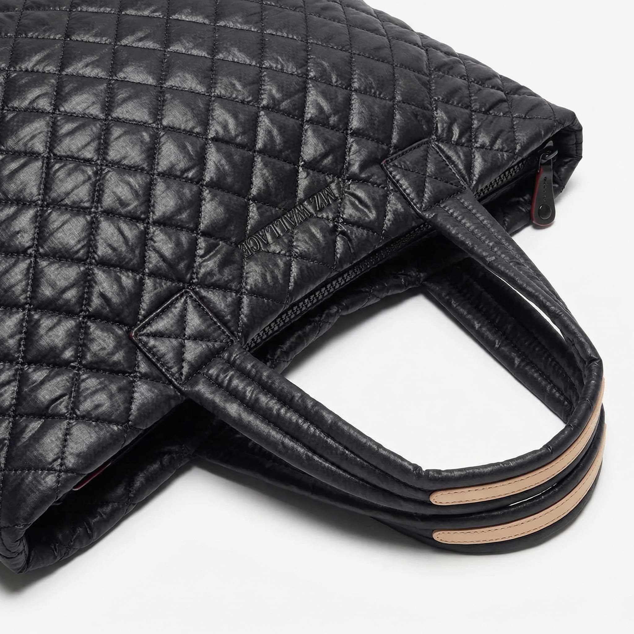 A close-up of a black quilted leather tote bag with two handles and beige accent strips near the handles, placed on a white surface.
