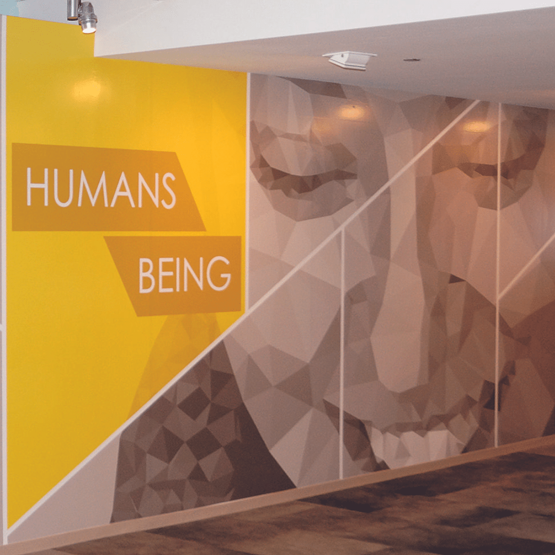 Yellow and brown geometric wall mural with the words "HUMANS BEING" and an abstract illustration of a person's face.