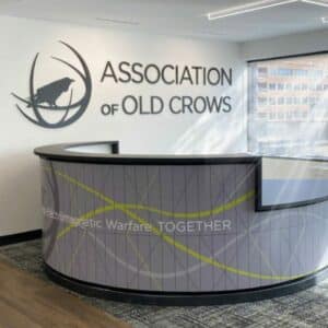 Reception area of the Association of Old Crows with a modern desk and logo on the wall, featuring text about electromagnetic warfare.