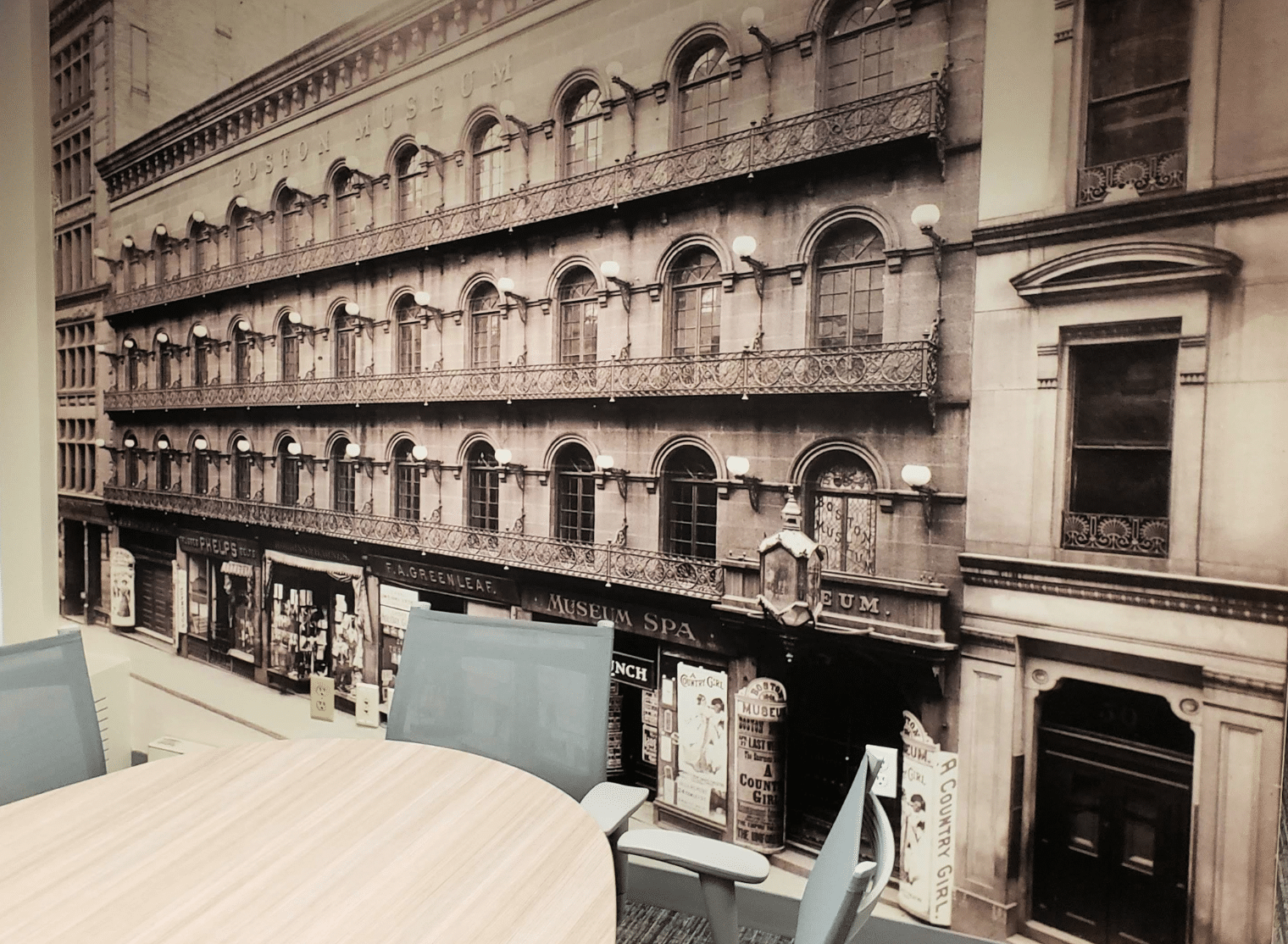 A meeting room with modern chairs and table, featuring a large wall mural of an old multi-story building with ornate balconies and storefronts.