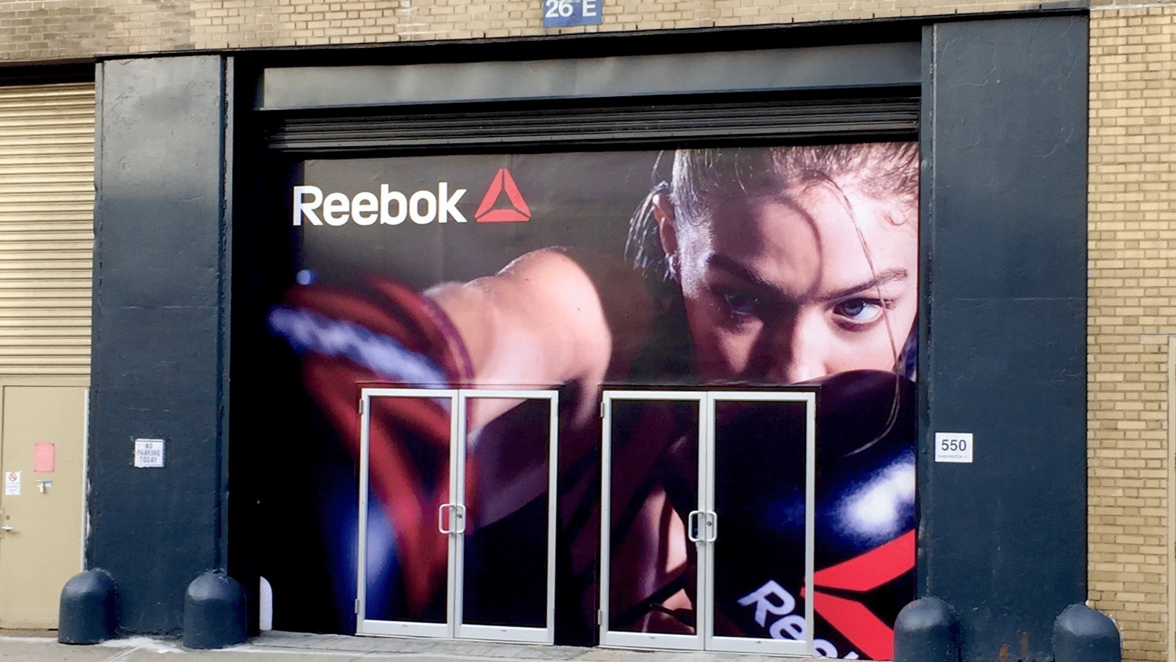 A gym entrance with a large Reebok advertisement showing a close-up of a person in boxing gloves, mid-punch, on the front wall.