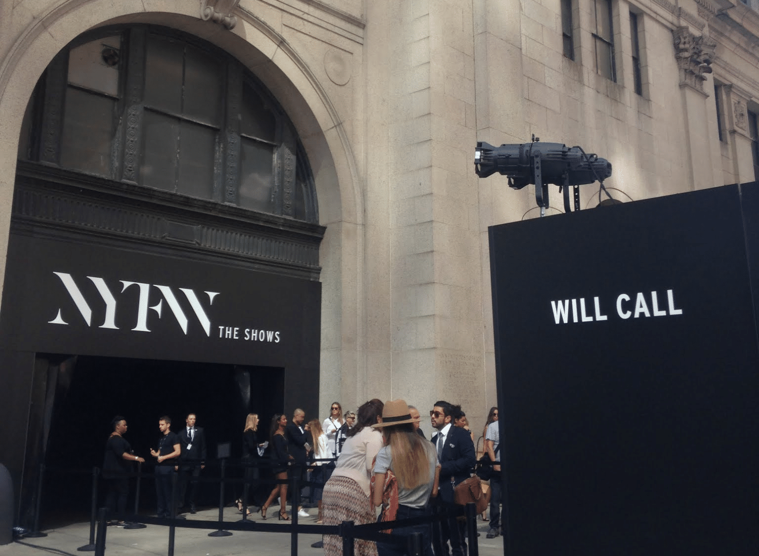 People stand in line outside a building with large signs reading "NYFW THE SHOWS" and "WILL CALL" during New York Fashion Week.